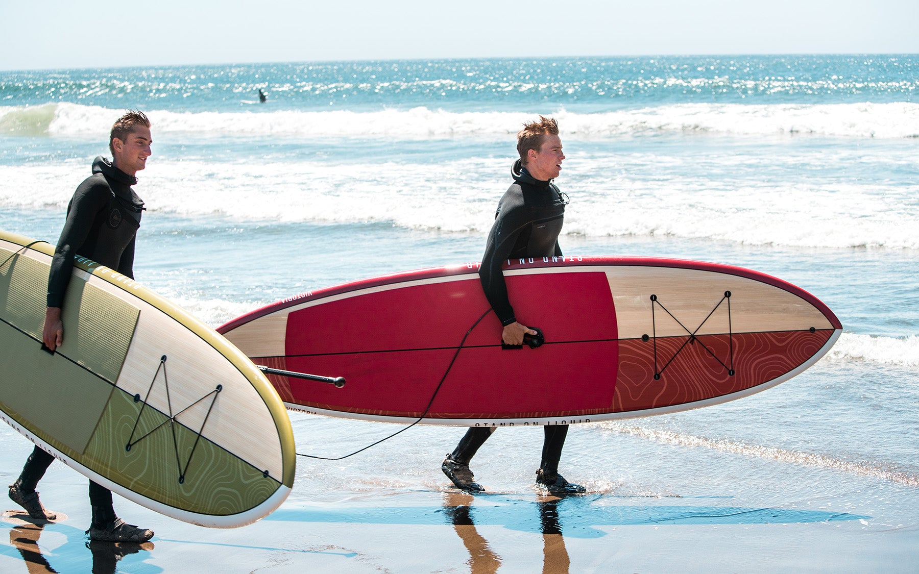 Surfers holding Stand on Liquid Victoria and Hudson stand up paddle boards at ocean with leashes attached